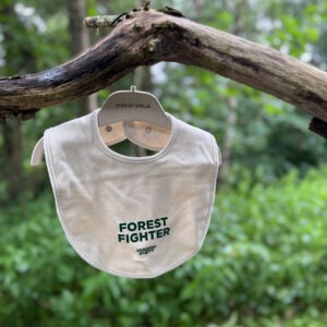 Baby bip i naturfarvet stof med grønt Forest Fighter-tryk hænger på en gren i skoven