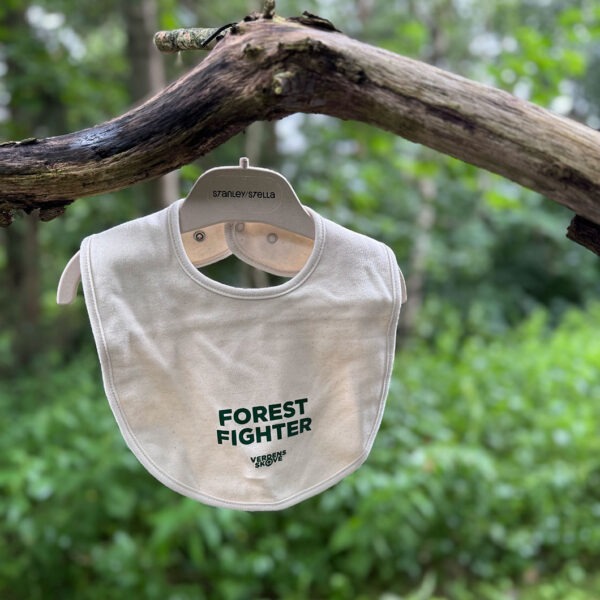 Baby bip i naturfarvet stof med grønt Forest Fighter-tryk hænger på en gren i skoven