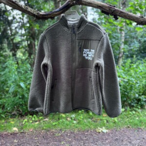 Fleecetrøje med lynlås i gråbrun fleece med “May the Forest Be With You”-tryk på brystet - vist hængende på en gren langs en skovsti