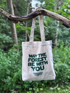 Hvid mulepose med teksten “May the Forest Be With You” hænger fra en gren i skoven