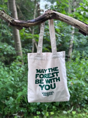 Hvid mulepose med teksten “May the Forest Be With You” hænger fra en gren i skoven