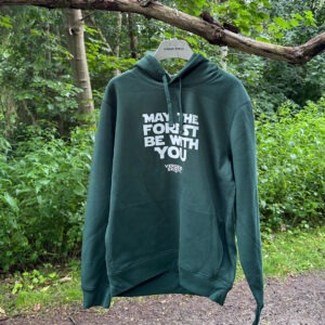Grøn hoodie med hvidt “May the Forest Be With You”-tryk på forsiden - set hængende på en gren langs en sti i skoven