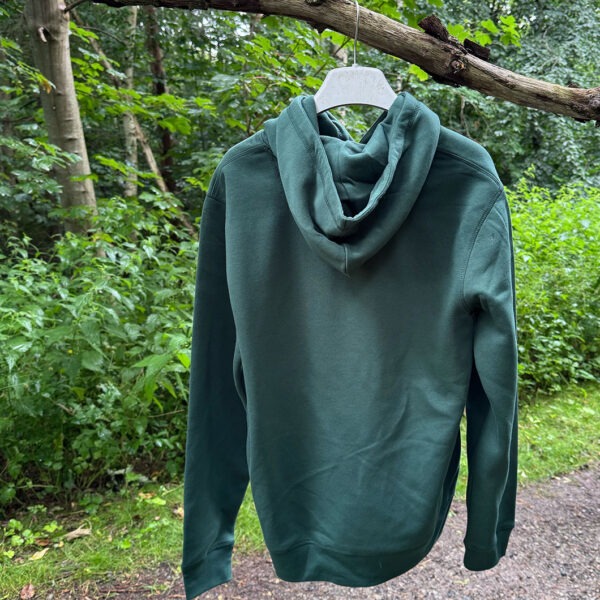 Hoodie grøn, vist bagfra med hætte og ensfarvet ryg - set hængende på en gren ved en skovsti