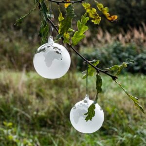 Mundblæst julekugle i høj kvalitet glas med verdenskort hænger på en gren med grønne egeblade i naturen